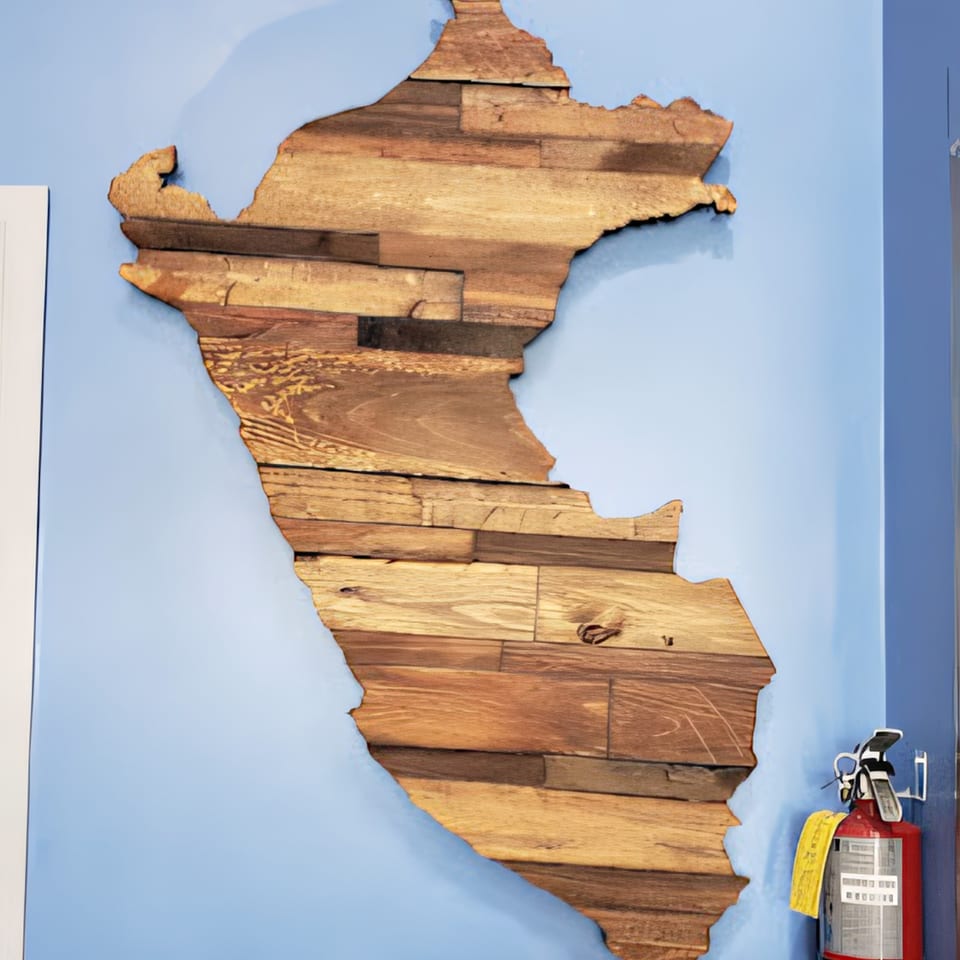 A wooden map of Peru hangs on a light blue wall next to a red fire extinguisher.