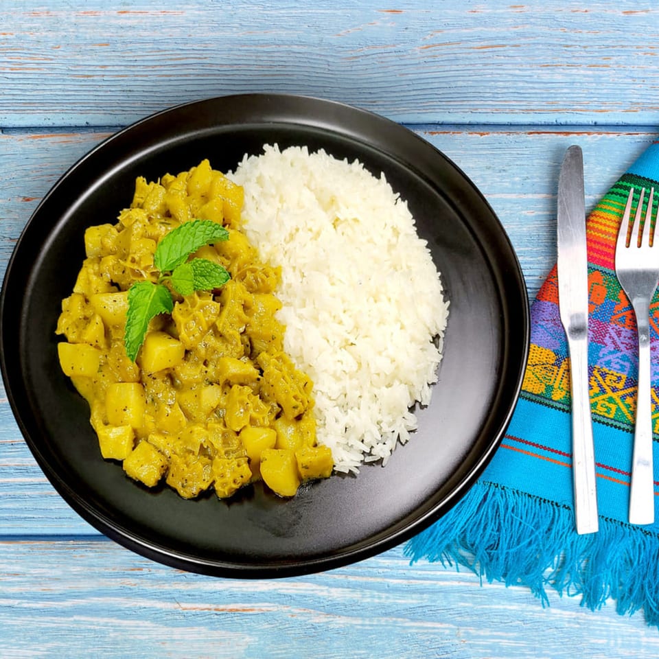 Peruvian tripe stew with potatoes and rice, garnished with mint, on a black plate.