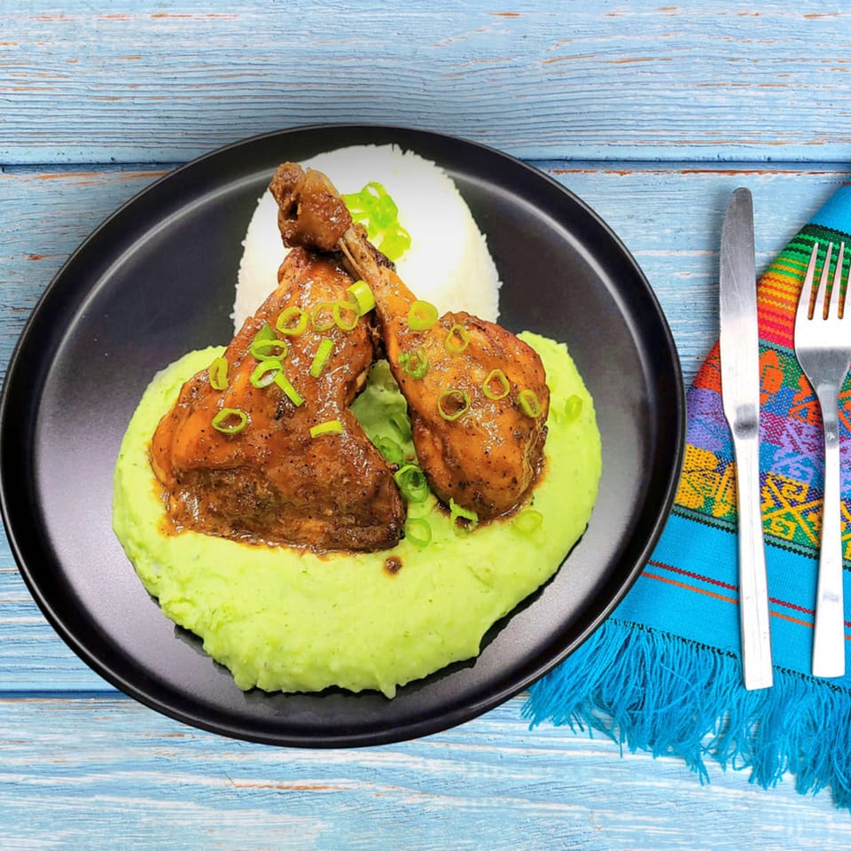 Peruvian chicken drumsticks with green mashed potatoes and rice on a black plate.