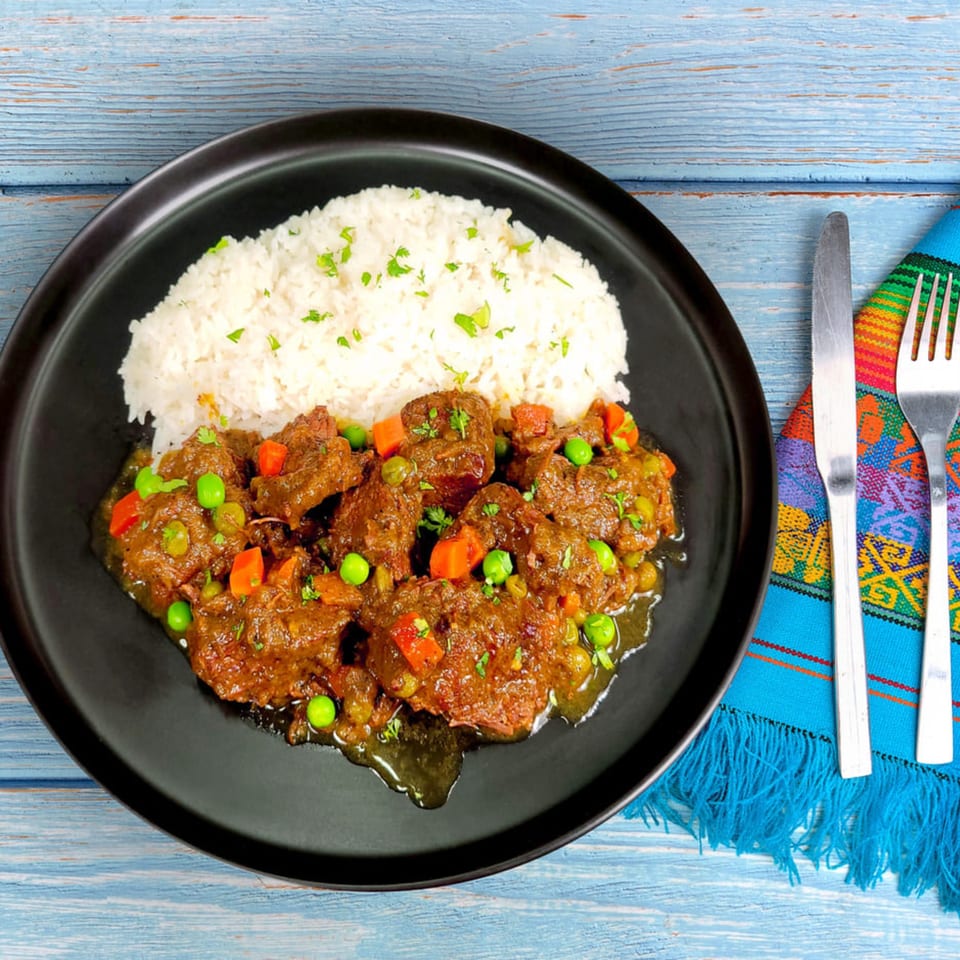 Peruvian seco de res with rice, peas, and carrots on a black plate with a colorful napkin.
