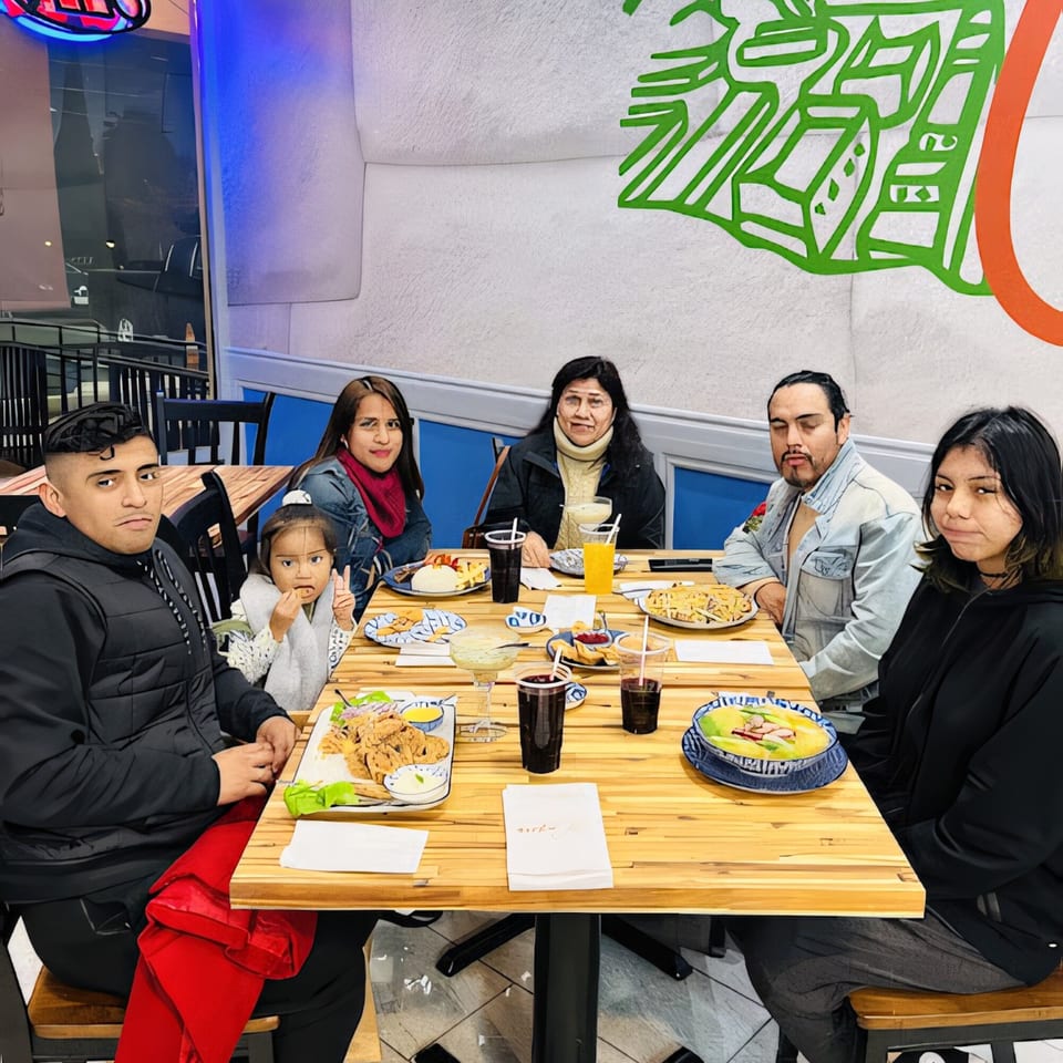 A family of six, including a young child, enjoys Peruvian dishes and drinks at a wooden table.