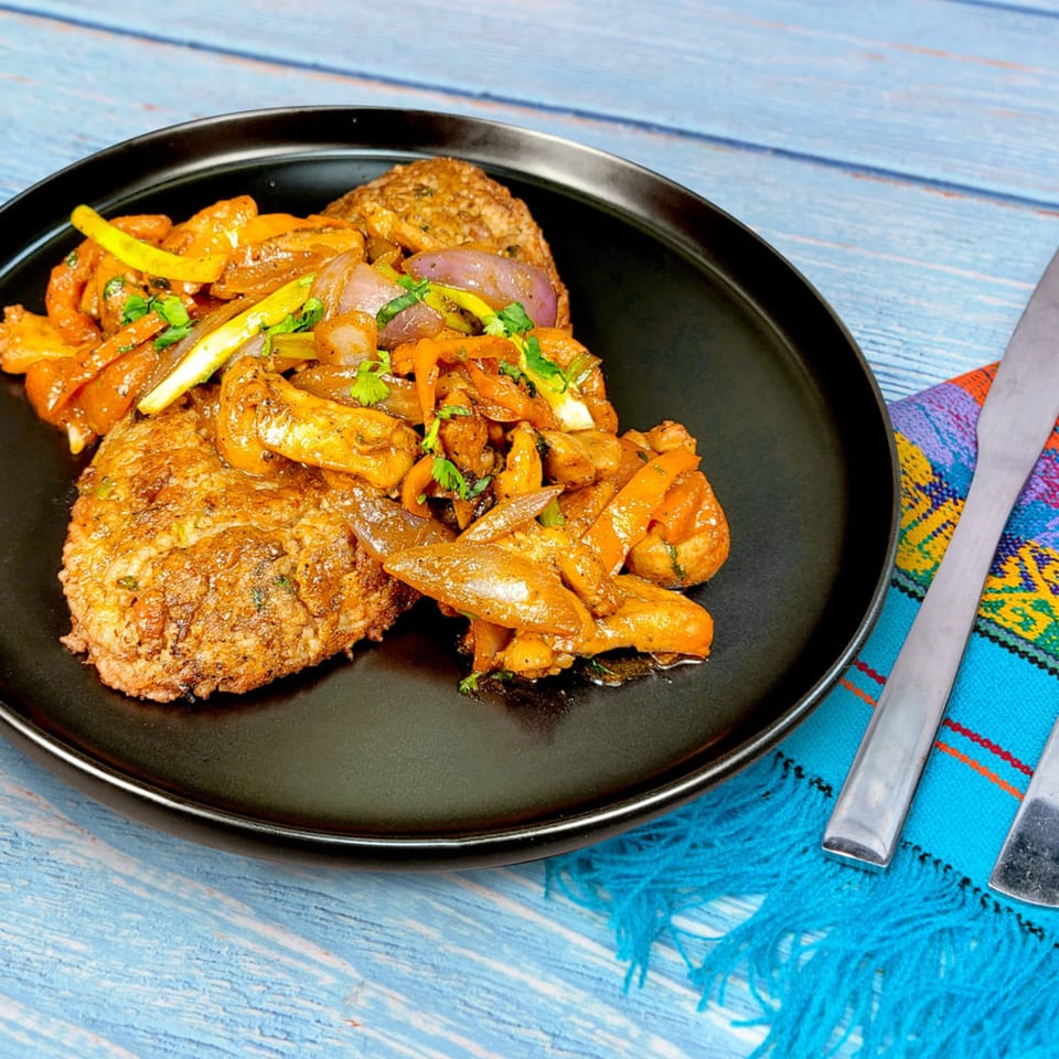 Peruvian dish with meat, sautéed vegetables, and onions on a black plate with colorful placemat.