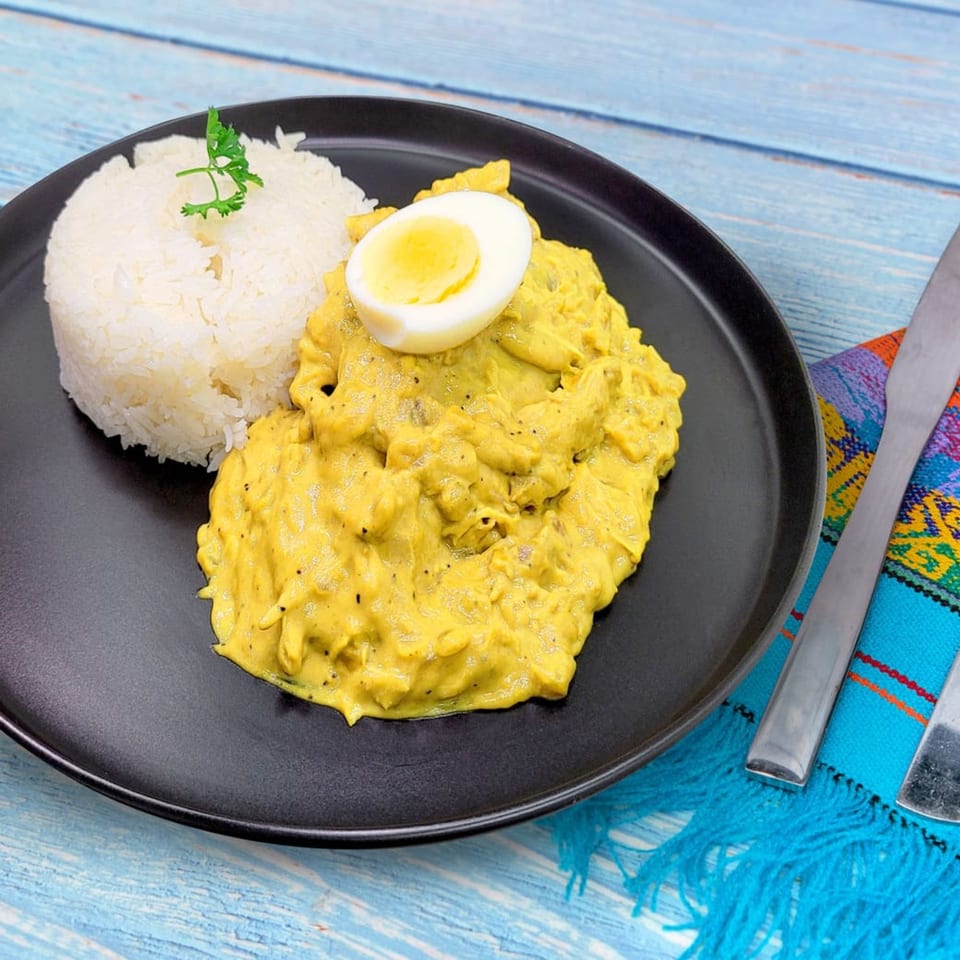 Aji de Gallina, a Peruvian chicken stew, with rice and a hard-boiled egg on a black plate.