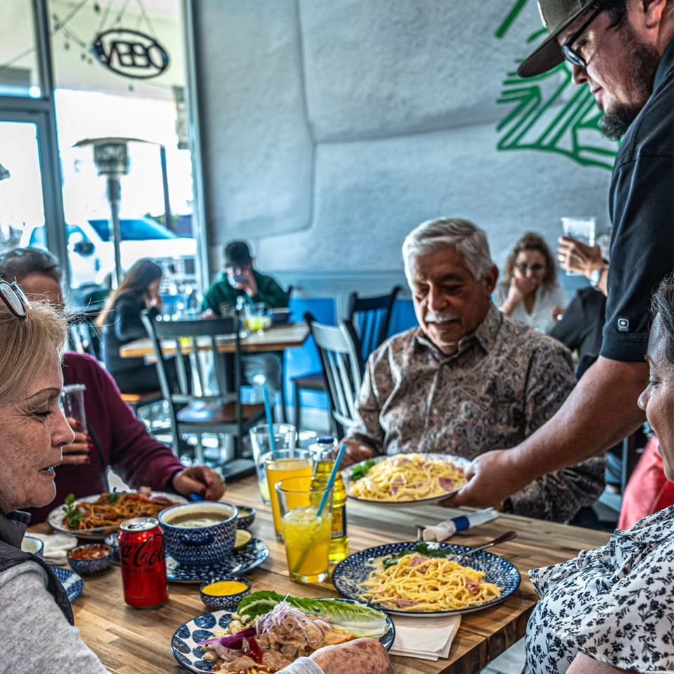 A server delivers a plate of spaghetti to a man at a table in Cuzco's Peruvian Restaurant.