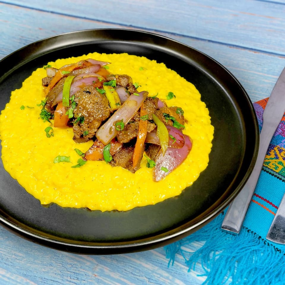 Peruvian Lomo Saltado, stir-fried beef with onions and peppers, served over yellow rice on a black plate.